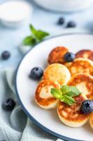 Käsepfannkuchen, Krapfen oder Syrniki mit Blaubeere, Physalis und Joghurt, blauer Hintergrund. Gesundes und leckeres Frühstück. foto