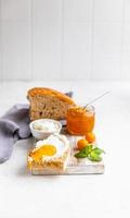 In Scheiben geschnittenes hausgemachtes Brot mit Ricotta oder Hüttenkäse und Orangenmarmelade auf hellem Hintergrund. leckeres Frühstück. High-Key-Fotografie. foto