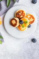 Hüttenkäsepfannkuchen, süße Quarkkrapfen mit Blaubeere und Physalis, konkreter Hintergrund. Syrniki mit Marmelade und Beeren für ein gesundes Frühstück. foto