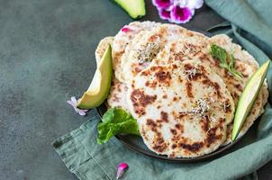 Hausgemachtes Chapati- oder Roti-Fladenbrot mit grüner Salatmischung, Avocado und Sprossen, Betonhintergrund. frisch gebackenes indisches Fladenbrot. foto