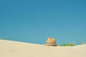 Strohhut auf dem Sand am Strand gegen den blauen Sommerhimmel, Nahaufnahme, Platz für Text kopieren. ein schöner sonniger Tag. Urlaub, Sommerkonzept foto