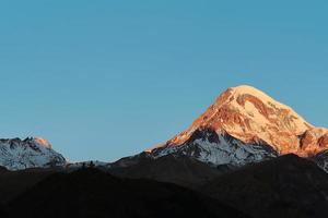 die spitze des berges kasbek aus dem hohen kaukasus, beleuchtet von der aufgehenden sonne, stepantsminda, georgia tourismus und erholung in den bergen foto