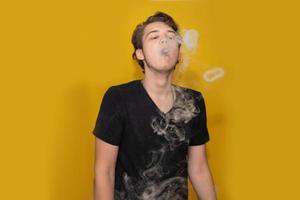 das Konzept der Popularisierung des Dampfens. Der dampfende junge Mann lässt einige Dampf- oder Rauchringe aus. Junger Mann löst Dampfringe aus seinem Mund. foto