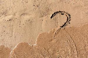 Fragezeichenzeichen am Sandstrand nahe dem Meer. konzept von dilemma, antwort und frage foto