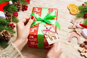 Draufsicht der weiblichen Hand binden Neujahrsgeschenk auf festlichem Holzhintergrund. Tannenbaum und Feiertagsdekorationen. Weihnachtszeit-Konzept foto