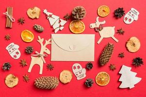 Blick von oben auf den Handwerksumschlag, roter Hintergrund mit festlichen Spielsachen und Weihnachtssymbolen, Rentieren und Neujahrsbäumen. Urlaubskonzept foto
