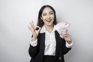 Aufgeregte asiatische Geschäftsfrau, die einen schwarzen Anzug trägt und eine ok-Handgeste gibt, die von einem weißen Hintergrund isoliert wird foto