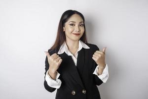 Aufgeregte asiatische Geschäftsfrau im schwarzen Anzug gibt Daumen hoch Handgeste der Zustimmung, isoliert durch weißen Hintergrund foto