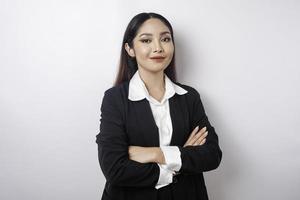 Porträt einer selbstbewusst lächelnden asiatischen Chefin mit schwarzem Anzug, die mit verschränkten Armen steht und isoliert auf weißem Hintergrund in die Kamera schaut foto