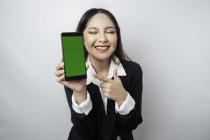 Eine glückliche junge Geschäftsfrau trägt einen schwarzen Anzug und zeigt Kopienraum auf ihrem Telefon, das durch weißen Hintergrund isoliert ist foto