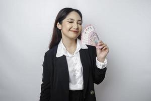 eine glückliche junge geschäftsfrau trägt einen schwarzen anzug und hält bargeld in indonesischer rupiah, das durch weißen hintergrund isoliert wird foto