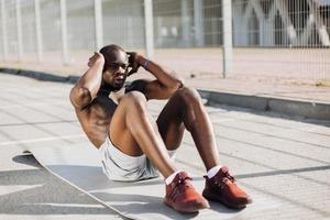 Der Afroamerikaner trainiert seine Bauchmuskeln, die draußen auf dem Boden liegen foto