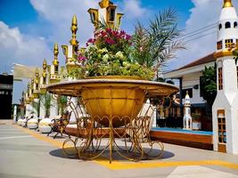 großer blumentopf mit goldenen eisenschnitzereien, architektur im arabischen stil, bunte blumen wachsen, hellblaue wolken. foto