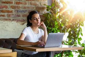 Frau, die in einem Café am Laptop arbeitet. junge Frau, die an einem Laptop arbeitet. schöne junge frau, die mit laptop vom café arbeitet. attraktive Frau, die in einem Café mit einem Laptop sitzt foto