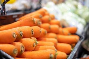 Bündel Karotten, viele orangefarbene Karotten, die auf einem schwarzen Regal im Supermarkt platziert sind. in der Lebensmittelzone aus landwirtschaftlichen Produkten im Kaufhaus, Seitenansicht foto