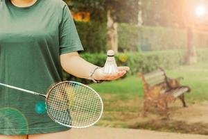 Weiße cremefarbene Badminton-Federbälle und Badmintonschläger zur Hand, verschwommene Baumhintergrundideen für Sport in einem gesunden Park. foto