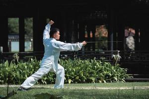 junger mann, der traditionelles tai chi-schwert, tai ji im park für gesundes, traditionelles chinesisches kampfkunstkonzept auf natürlichem hintergrund übt. foto