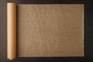 Eine Rolle ungefaltetes braunes Pergamentpapier zum Backen von Speisen auf dunklem Hintergrund, Draufsicht. foto