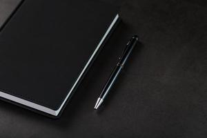 Schreibtisch mit schwarzem Notizblock und Stift auf schwarzem Hintergrund. foto