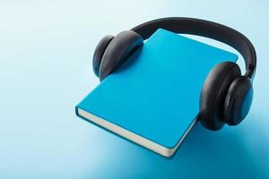 Kopfhörer werden auf einem Buch in einem blauen Hardcover auf blauem Hintergrund getragen, Ansicht von oben. foto