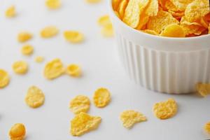 weiße Tasse mit goldenen Cornflakes, isoliert auf weißem Hintergrund. Hopya zerbröckelte um die Tasse herum. Sicht von oben foto