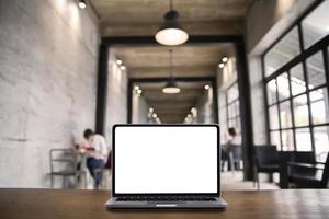 laptop-computer mit leerem weißem bildschirm auf tisch mit modernem arbeitsplatzhintergrund, soziales distanzierungskonzept foto