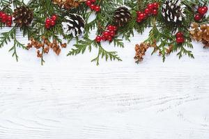 Grenze von Weihnachtsbaumzweigen, Tannenzapfen, Blumen und roten Beeren auf weißem Holzhintergrund, Kopierraum foto
