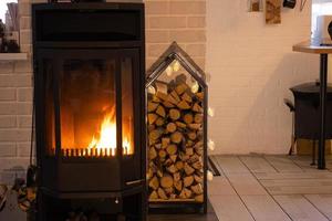 Schwarzer Metallofenkamin mit Holz in einem Holzstapel - das Innere eines privaten Dorfhauses. heizung und heizung des hauses mit brennholz, die wärme des feuers aus dem herd. foto