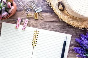 Die flache Lage des femininen Vintage-Sommerkonzepts mit einem offenen rosa Spiralnotizbuch, einem Strandhut, Holzclips und dekorativen Blumen. foto