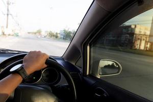 Hand von Menschen hält das Lenkrad nach rechts. tagsüber im auto auf der leeren straße fahren. verschwommen von der stadt neben der straße in thailand. foto