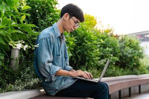 Bild eines asiatischen Jungen, der auf dem Schulcampus sitzt und Computer benutzt foto