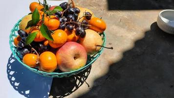 tropische früchte im grünen korb auf weißem hintergrund und freiliegendem zement zwischen schatten foto