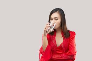 asiatische Frau in einem roten Satin-Nachthemd, das nachts ein Glas Wasser trinkt. foto