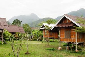 Blick auf Holzhäuser und Garten vor dem Hintergrund der Berge bei bewölktem Wetter. pai, provinz mae hong bald, thailand. foto