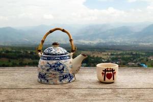 chinesische teekanne und tasse mit grünem tee auf einem holztisch vor dem hintergrund der malerischen berglandschaft. pai, thailand. foto