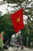 hue, vietnam - 04. februar 2018. vietnamesische flagge nahaufnahme mit blick auf eine straße der stadt mit motorradfahrern. foto