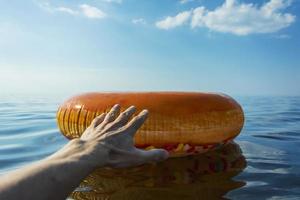 die hand einer person greift um hilfe zu einem aufblasbaren kreis zum schwimmen auf dem meerwasser, sommerstrandurlaub foto