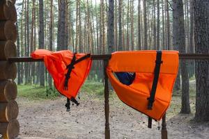 Am Geländer eines Waldhauses hängen leuchtend orange Schwimmwesten für Kinder und Erwachsene foto