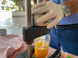 Bei der Herstellung von frisch gepresstem gelben Orangensaft drückt ein Mann in einem Hotel in einem warmen östlichen tropischen Land im südlichen Paradies mit seinen Händen Saft in ein Glas foto