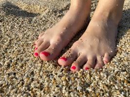 weibliche beine, füße mit einer schönen roten pediküre vor dem hintergrund des krümeligen gelben goldenen sandes im urlaub am strand in einem warmen tropischen östlichen paradies land im süden foto