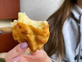 Frauenmädchen hält mit ihrer Hand ein gebissenes gelbes köstliches gebratenes Pastetchen mit Kartoffeln foto