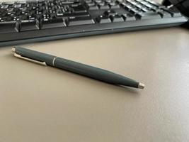 Automatischer grüner Kugelschreiber zum Schreiben auf dem Schreibtisch mit Computertastatur. geschäftliche Arbeit