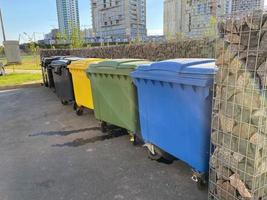 Schwarze, gelbe, grüne und blaue große moderne Kunststoffbehälter für die getrennte Sammlung und anschließende ökologische Verwertung von Abfällen in einem neuen Stadtteil foto
