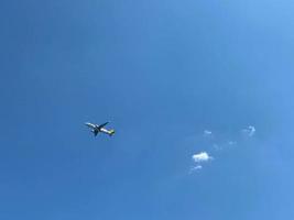 Ein weißes Flugzeug, das in einem klaren, hellblauen Himmel fliegt foto