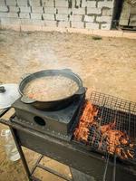 Kochen auf offenem Feuer. Auf dem Grill wird ein Feuer angezündet und es gibt einen Kessel mit Pilaw, daneben liegt ein Grill. Mahlzeiten im Freien. Reispilaf foto