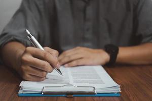Person Mann mit Stift schreiben Vertrag Geschäftsdokument und Unterschrift Papierkram Versicherung oder Anwalt auf dem Schreibtisch.