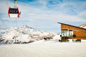 weiße, rote, geschlossene skiliftkabine mit skifahrern und weißem, dramatischem, schneebedecktem berghintergrund. Skigebiet wiedereröffnet. georgien winterferien in gudaur. Kobi Pisten Café und Umgebung foto