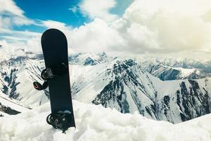 schwarzes Snowboard im Schnee mit weißen Bergen im Hintergrund. konzept des endes der skisaison.gudauri. Sakartvelo. Georgien Winterurlaub Panorama foto