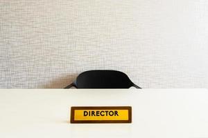 Büroplatte aus Holz für den Direktor auf weißem, glänzendem Tisch mit leerem Stuhl im Zimmer foto