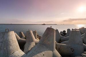 Schlepper, der im Meer segelt, um das Schiff zum Hafen zu schleppen. Tetrapoden-Wellenbrecher im Hafen. schöner Sonnenuntergang über dem Pier. foto